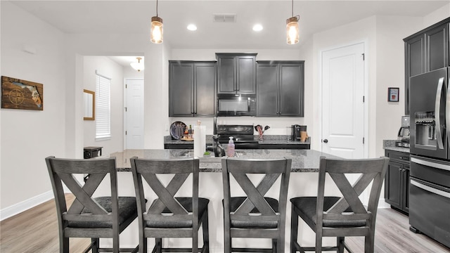 kitchen featuring hanging light fixtures, black appliances, a breakfast bar area, and an island with sink