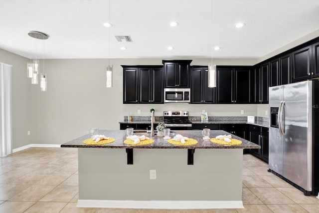 kitchen with dark stone countertops, appliances with stainless steel finishes, an island with sink, and light tile patterned floors