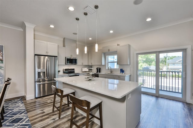 kitchen with hanging light fixtures, ornamental molding, appliances with stainless steel finishes, hardwood / wood-style flooring, and a center island