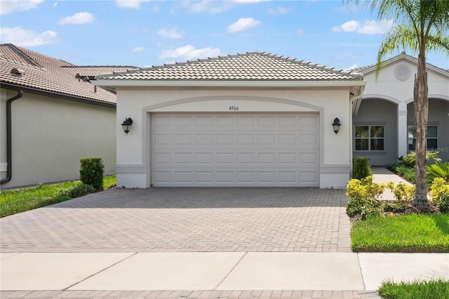 view of front of property with an attached garage, a tile roof, decorative driveway, and stucco siding