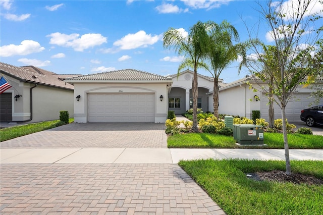 mediterranean / spanish-style house with a garage, a tiled roof, decorative driveway, and stucco siding