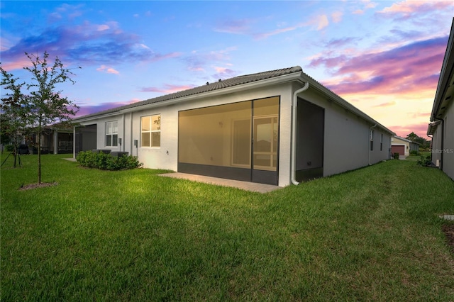 back of property at dusk with a lawn and stucco siding