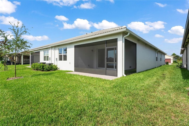 rear view of house with a sunroom, a lawn, and stucco siding