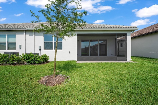 rear view of property featuring a sunroom, a tile roof, a lawn, and stucco siding