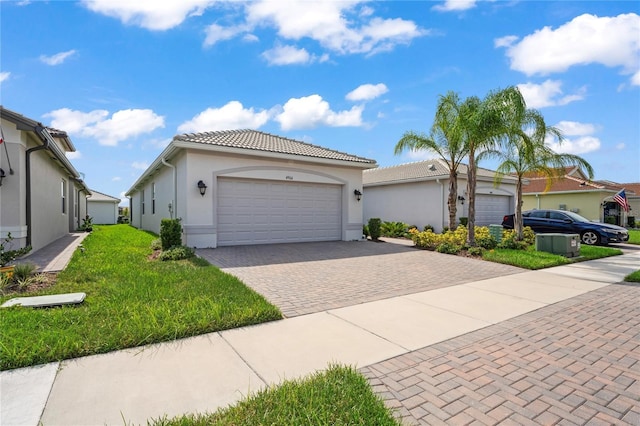 view of front of house featuring stucco siding, a tiled roof, an attached garage, decorative driveway, and a front yard