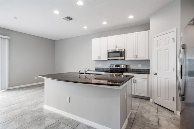 kitchen with sink, white cabinetry, light tile patterned floors, appliances with stainless steel finishes, and an island with sink