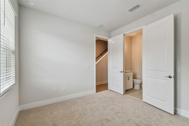 unfurnished bedroom featuring light colored carpet and ensuite bath