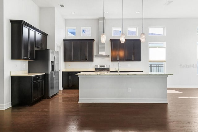 kitchen with a kitchen island with sink, dark hardwood / wood-style floors, stainless steel appliances, light stone countertops, and pendant lighting