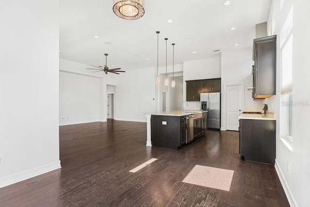 kitchen featuring an island with sink, hanging light fixtures, stainless steel appliances, dark brown cabinetry, and dark hardwood / wood-style floors