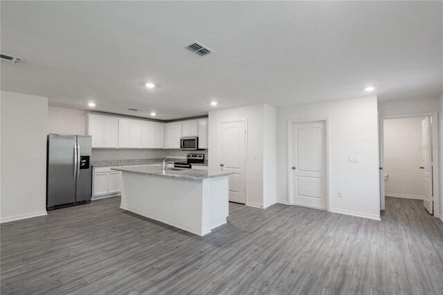 kitchen featuring appliances with stainless steel finishes, light hardwood / wood-style floors, light stone counters, an island with sink, and white cabinets