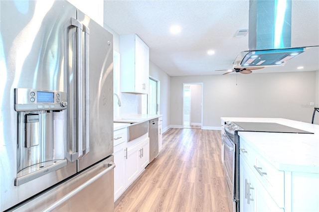 kitchen featuring light wood-type flooring, ceiling fan, appliances with stainless steel finishes, white cabinets, and island exhaust hood