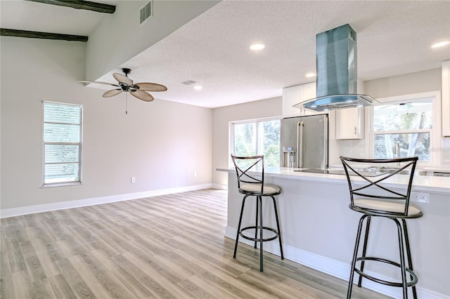 kitchen featuring a textured ceiling, a breakfast bar area, high quality fridge, island range hood, and white cabinets