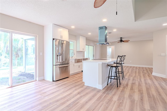 kitchen featuring ceiling fan, a kitchen island, high quality fridge, island range hood, and white cabinetry