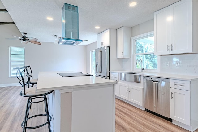 kitchen with white cabinets, light wood-type flooring, a textured ceiling, range hood, and stainless steel appliances