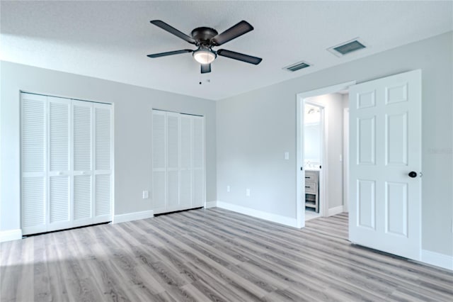 unfurnished bedroom with light wood-type flooring, ceiling fan, and multiple closets