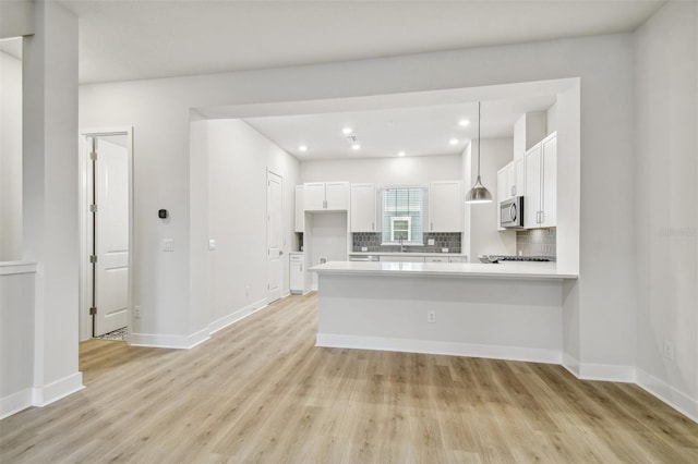 kitchen with hanging light fixtures, light wood-type flooring, tasteful backsplash, white cabinetry, and kitchen peninsula