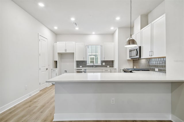 kitchen with kitchen peninsula, appliances with stainless steel finishes, pendant lighting, light hardwood / wood-style floors, and white cabinetry