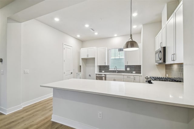 kitchen featuring sink, kitchen peninsula, decorative light fixtures, white cabinets, and appliances with stainless steel finishes