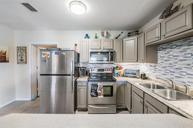 kitchen featuring backsplash, appliances with stainless steel finishes, sink, gray cabinets, and light tile patterned flooring