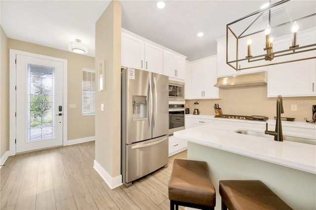 kitchen featuring hanging light fixtures, under cabinet range hood, white cabinets, and stainless steel appliances