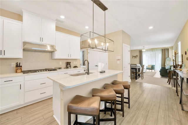 kitchen featuring a kitchen island with sink, light countertops, under cabinet range hood, pendant lighting, and a sink