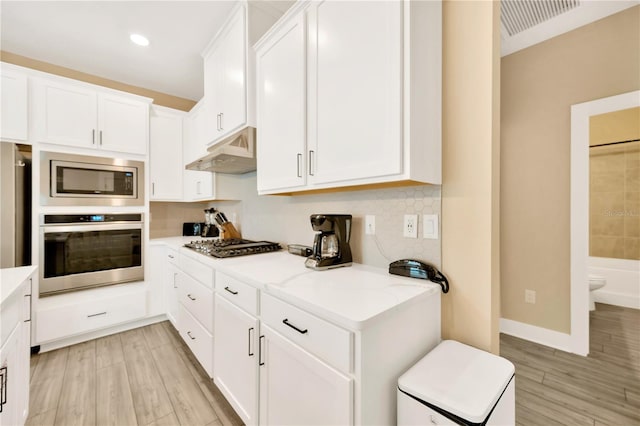 kitchen with appliances with stainless steel finishes, light stone counters, white cabinets, and light wood-type flooring