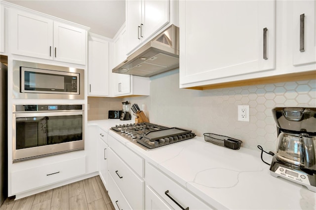 kitchen with white cabinets, decorative backsplash, light stone countertops, and stainless steel appliances