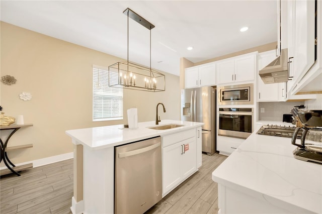 kitchen with a center island with sink, appliances with stainless steel finishes, hanging light fixtures, range hood, and a sink