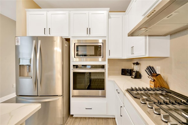 kitchen with stainless steel appliances, white cabinetry, under cabinet range hood, and light stone countertops