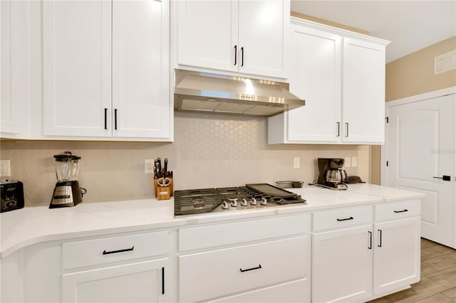 kitchen featuring light stone counters, stainless steel gas cooktop, tasteful backsplash, white cabinetry, and under cabinet range hood