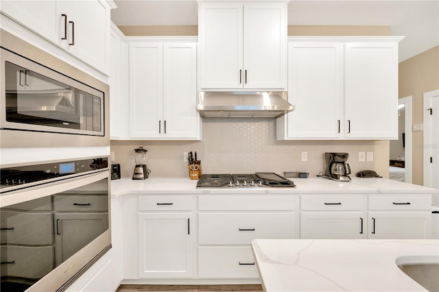 kitchen with stainless steel appliances, wall chimney range hood, light stone counters, and white cabinetry