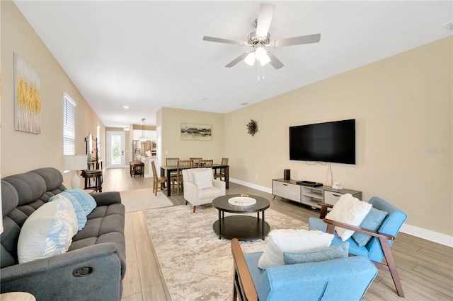 living room featuring light wood-type flooring, a ceiling fan, and baseboards