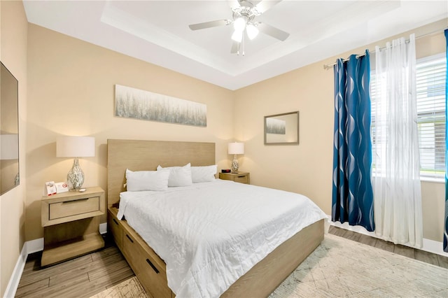 bedroom with ceiling fan, a raised ceiling, and light hardwood / wood-style flooring