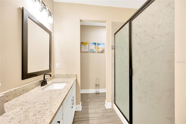 full bath with a stall shower, vanity, baseboards, and wood finished floors