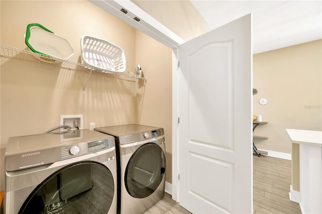 clothes washing area with wood finish floors, laundry area, baseboards, and washing machine and clothes dryer