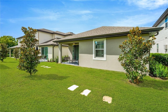 back of property with a shingled roof, a lawn, and stucco siding