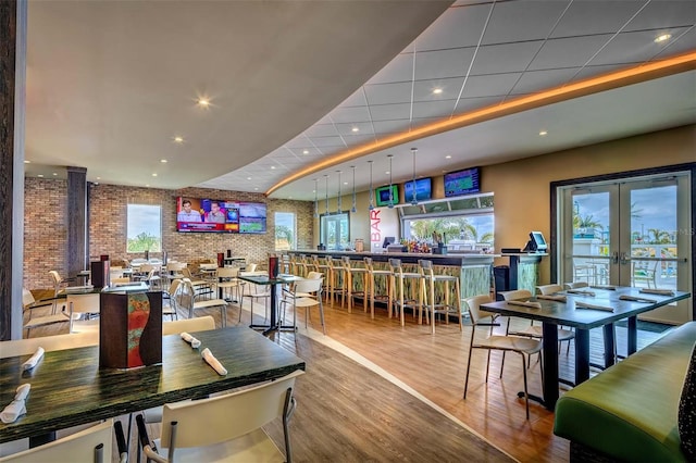 dining area featuring a drop ceiling, brick wall, hardwood / wood-style flooring, and french doors