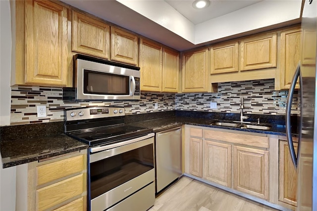 kitchen with dark stone counters, appliances with stainless steel finishes, sink, and light hardwood / wood-style flooring