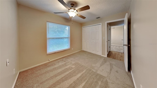 unfurnished bedroom with ceiling fan, a closet, light carpet, and a textured ceiling