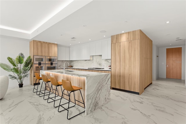 kitchen featuring white cabinets, a kitchen bar, a kitchen island with sink, and light tile patterned floors