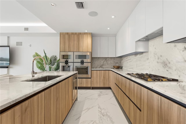 kitchen with stainless steel gas cooktop, white cabinetry, tasteful backsplash, sink, and light stone counters