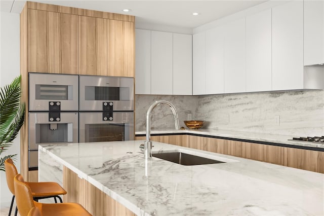 kitchen featuring white cabinets, a breakfast bar, light stone countertops, and tasteful backsplash