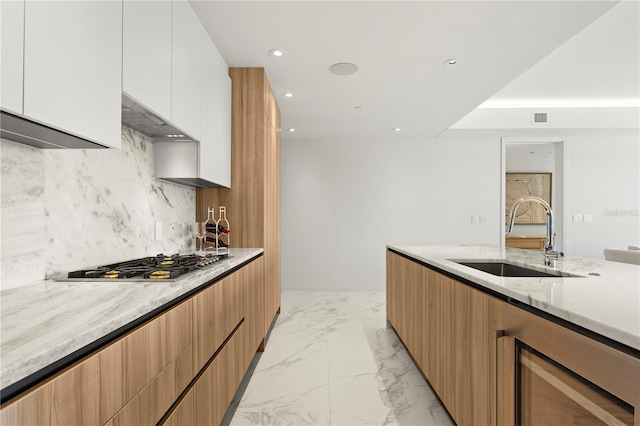 kitchen featuring sink, custom range hood, stainless steel gas stovetop, white cabinetry, and beverage cooler