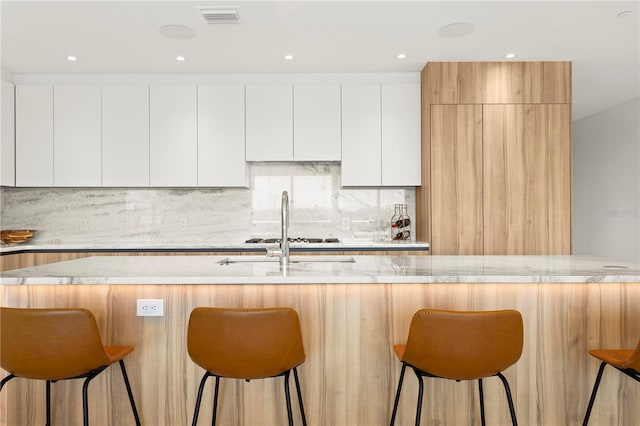 kitchen with light stone counters, white cabinetry, an island with sink, and a kitchen bar