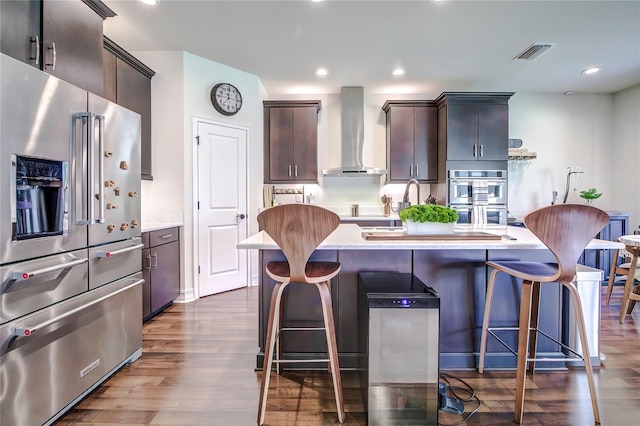 kitchen with hardwood / wood-style floors, a center island, dark brown cabinets, stainless steel appliances, and wall chimney range hood