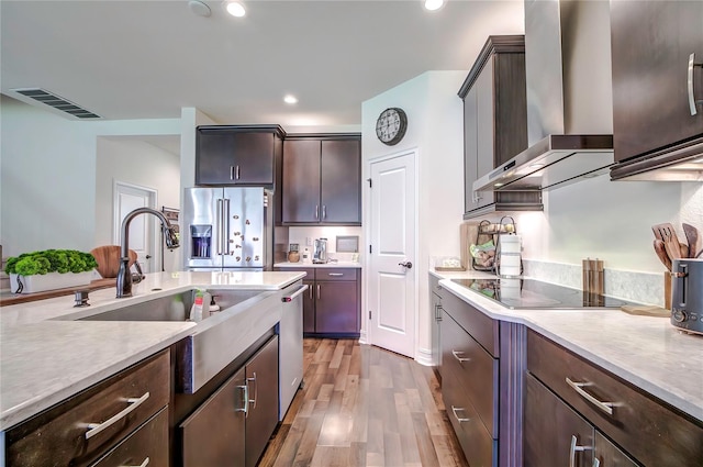 kitchen featuring appliances with stainless steel finishes, dark brown cabinets, sink, wall chimney range hood, and wood-type flooring