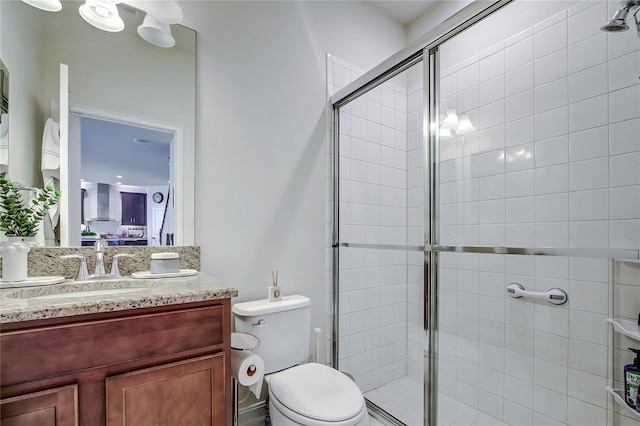 bathroom featuring a shower with door, toilet, and vanity