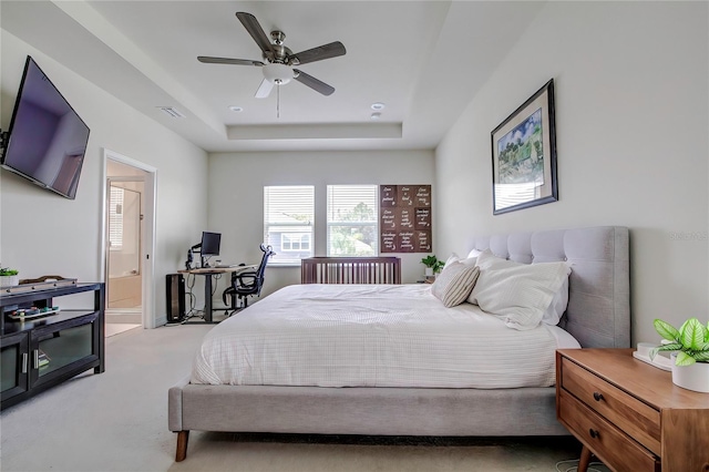 bedroom featuring ceiling fan, ensuite bath, light colored carpet, and a tray ceiling