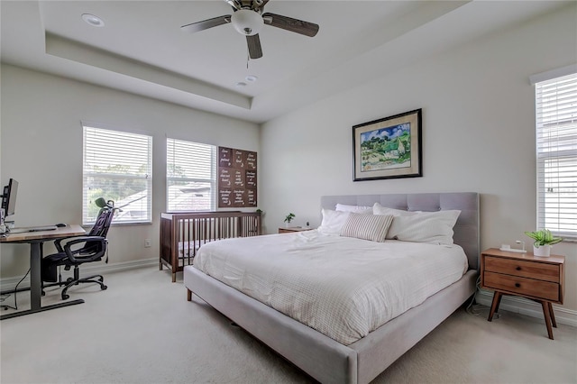 carpeted bedroom with ceiling fan, a raised ceiling, and multiple windows