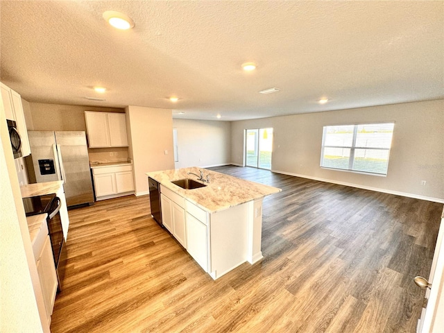 kitchen with a center island with sink, white cabinets, light wood-type flooring, black appliances, and a sink